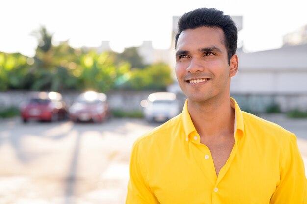 Happy young handsome Indian man thinking in the streets outdoors