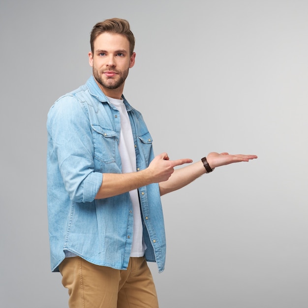 Happy young handsome man in jeans shirt pointing away standing  