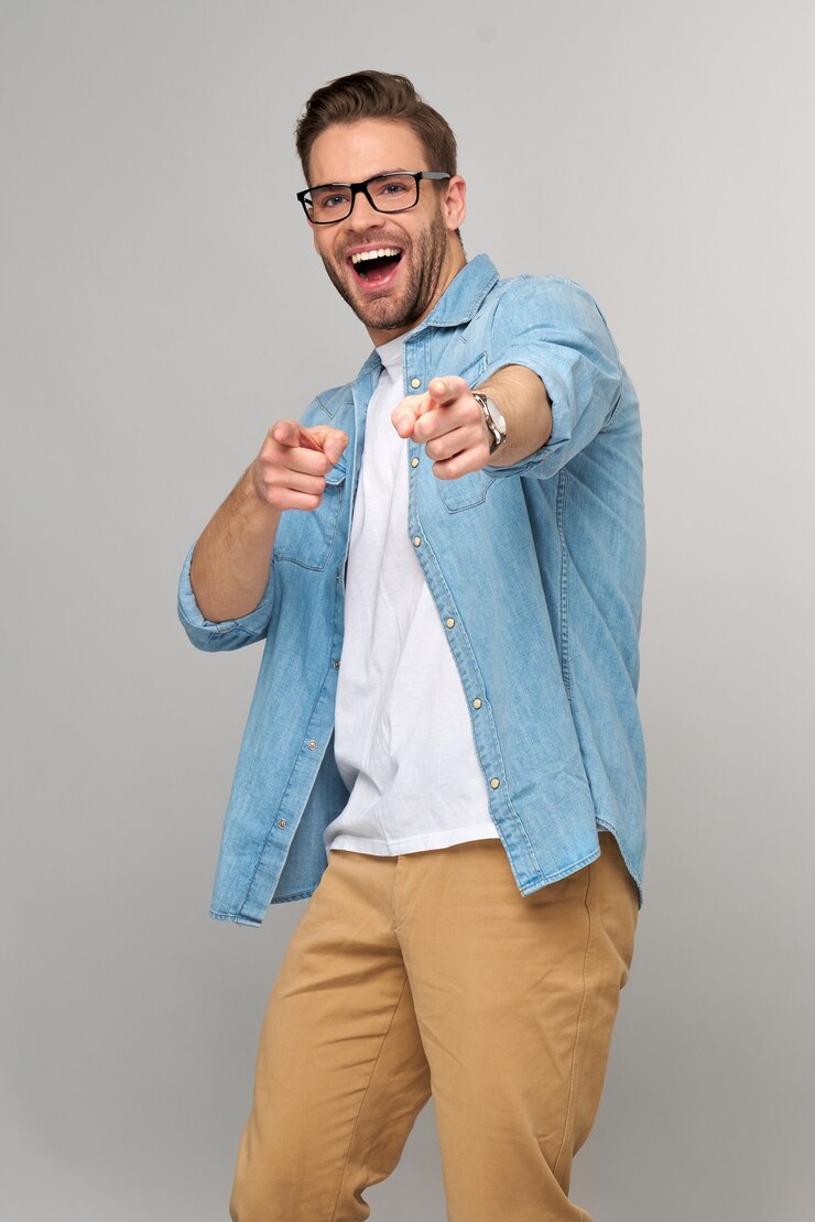 Photo happy young handsome man in jeans shirt pointing on camera standing against grey wall