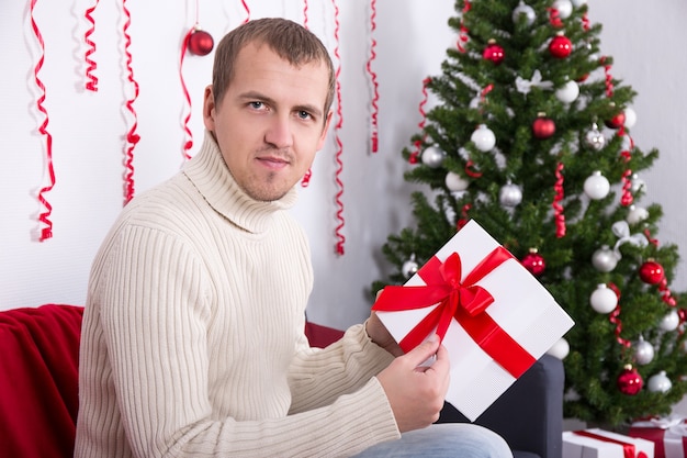 Счастливый молодой красавец открывает рождественский подарок в украшенной гостиной