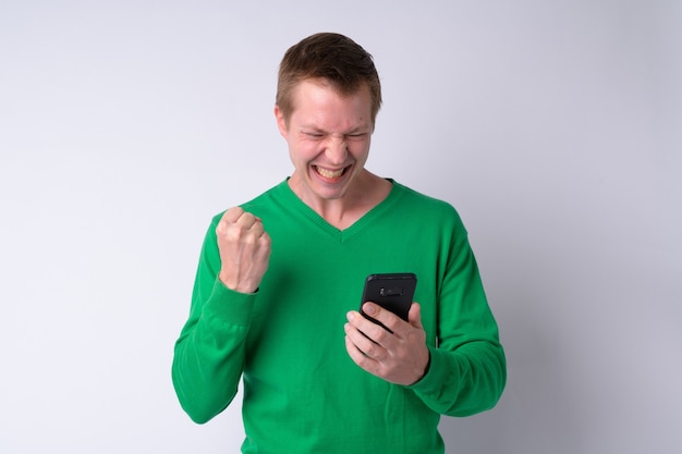 Happy young handsome man using phone and getting good news