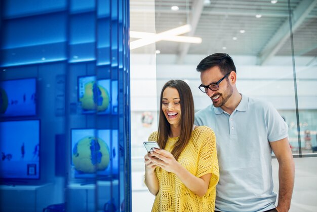 Happy young hipster attractive love couple holding and testing new mobile in a tech store.