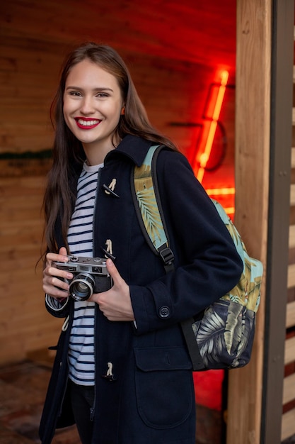 Happy young hipster woman holds retro photo camera. Having fun in the city with camera, travel photo of photographer.