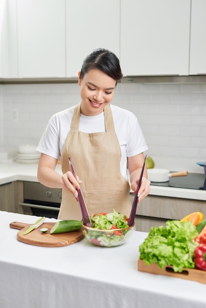 Happy young housewife mixing vegetable salad