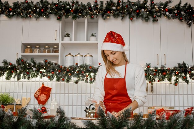 Felice giovane casalinga in grembiule rosso che decora i biscotti di natale in cucina