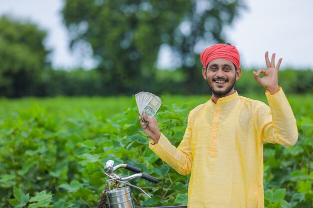 幸せな若いインドの農民が数え、お金を示しています