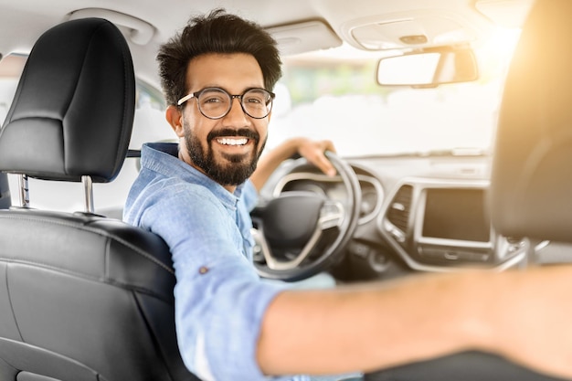 Foto un giovane indiano felice che impara a guidare seduto in auto