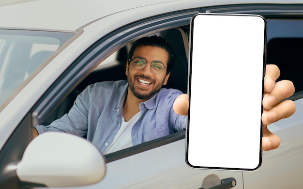 차에 앉아있는 동안 큰 빈 스마트폰을 보여주는 행복한 젊은 인도 남자