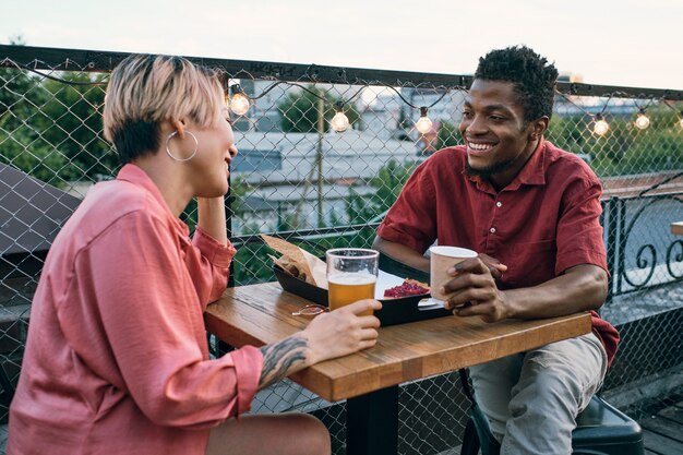 Happy young intercultural couple having drinks and snacks in outdoor cafe