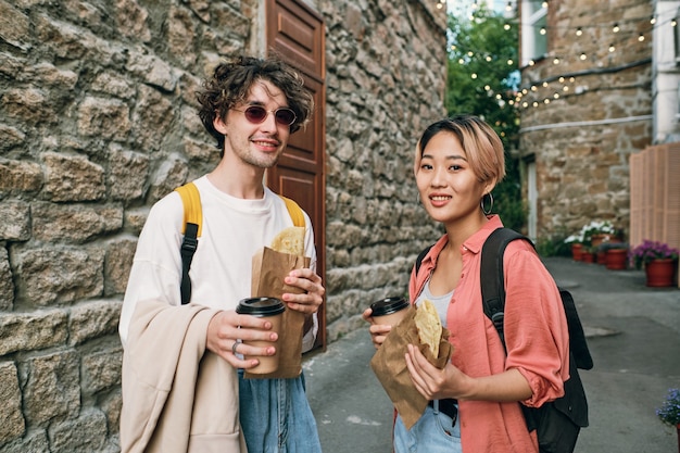 Happy young intercultural couple having fastfood with drinks