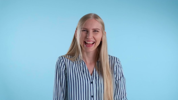 Happy young lady bursting in laughter on blue background. She has long blonde hair.