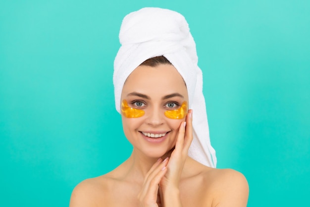 Happy young lady has collagen golden eye patches on face with towel