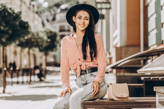 Happy young lady in a hat sitting in the street on sunny day