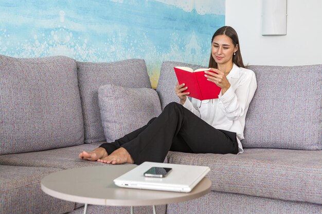 Happy young lady resting on sofa and reading book