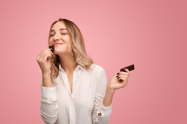 スタジオでおいしいチョコレートバーを嗅ぐ幸せな若い女性