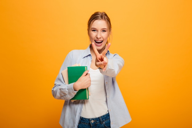 Happy young lady studen with peace gesture holding books.