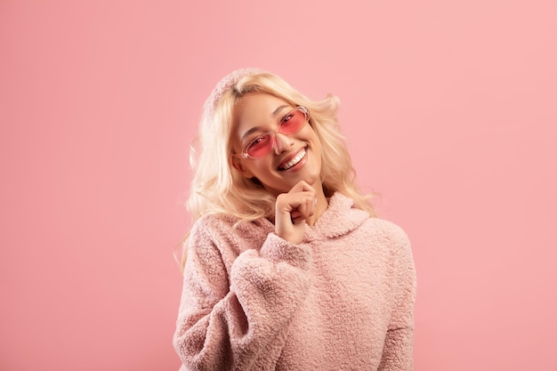 Happy young lady touching chin and smiling at camera wearing stylish colorful sunglasses and hoodie