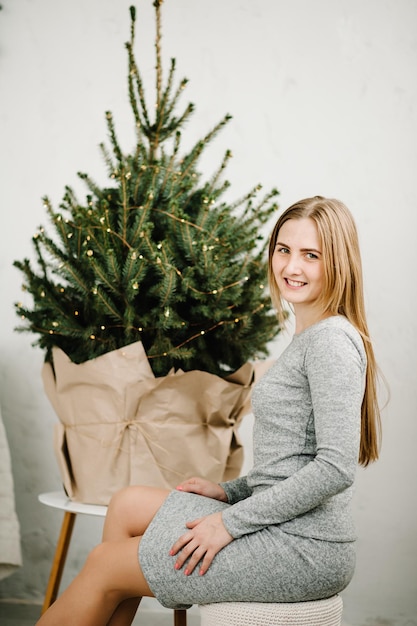 クリスマス ツリーの近くの長い髪を持つ幸せな若い女性新年の概念休日のお祝いと人々 の概念クリスマス インテリア背景にエレガントなドレスを着た女性