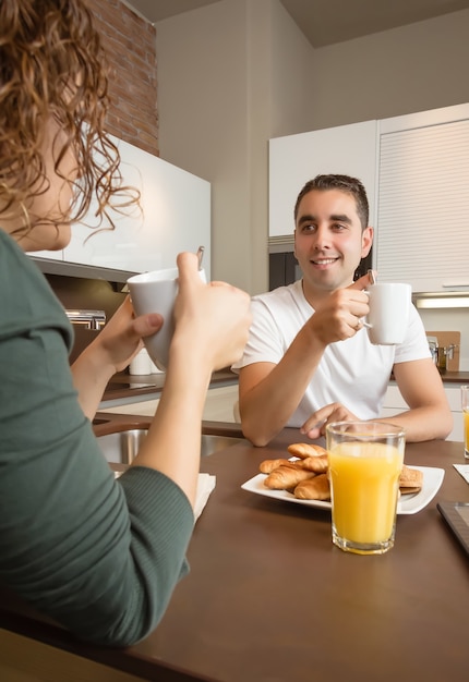 幸せな若い愛のカップルが話し、家庭の台所でおいしい朝食をとる