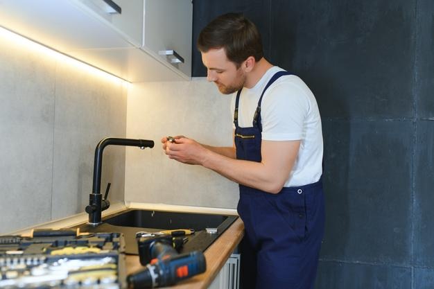 happy young male plumber fixing faucet in kitchen
