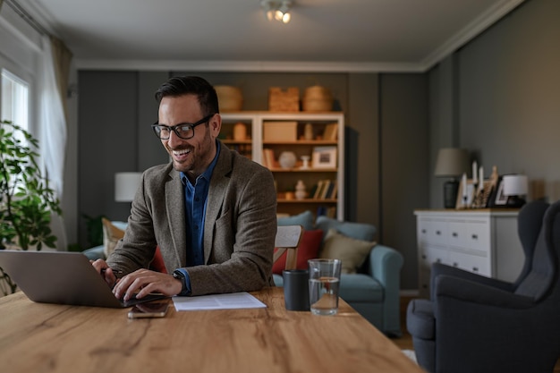 Happy young male professional in elegant suit typing email over laptop on desk in home office