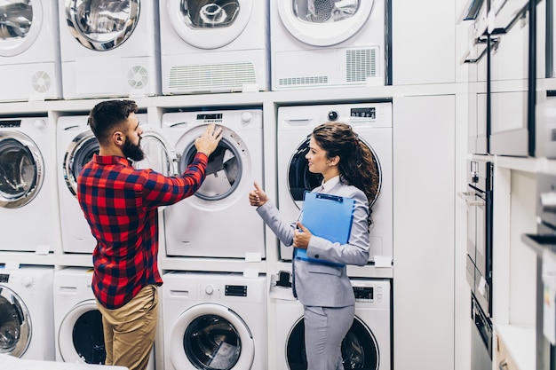 Happy young man choosing new washing machine for his home in\
modern appliances store.