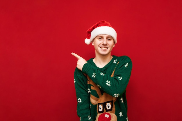 Happy young man in christmas clothes stands on red background looks into the camera