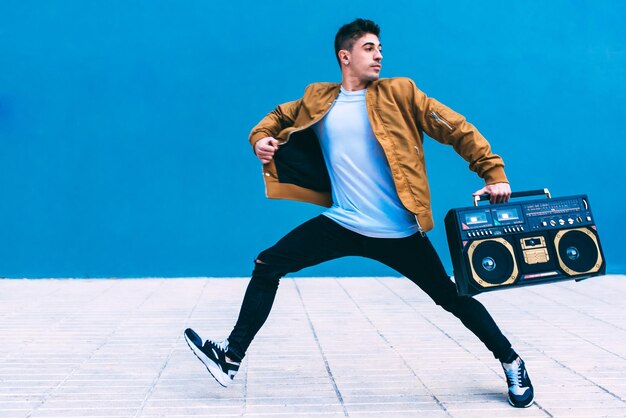 Happy young man dancing and jumping in the street with a vintage radio cassette stereo