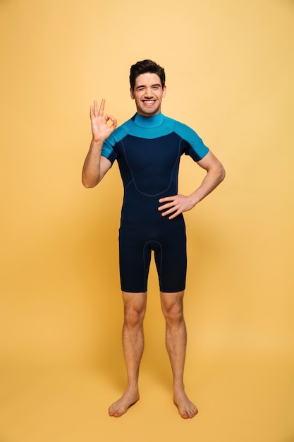 Happy young man dressed in swimsuit showing okay gesture.