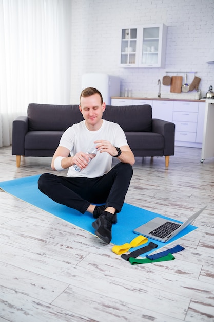 Il giovane felice beve l'acqua dopo l'allenamento online. fare sport in casa, stile di vita sano