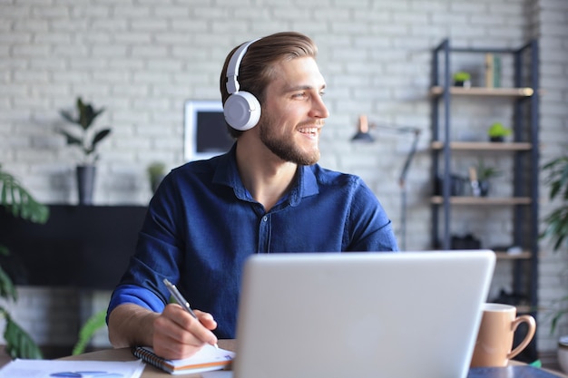 Happy young man in earphones working on laptop from home during self isolation.