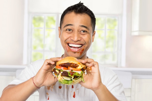 Happy young man eating a big burger