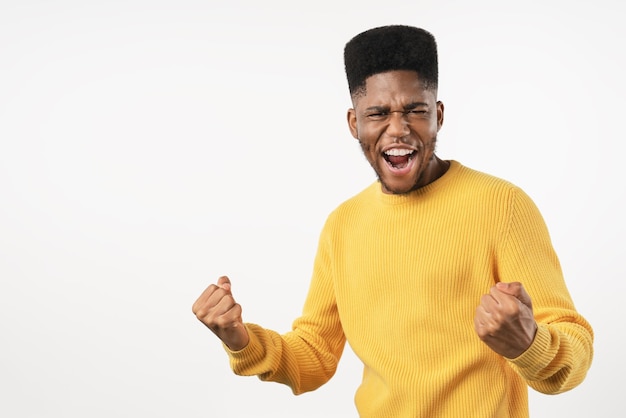 Happy young man gesturing winning and keeping mouth open while standing against white background