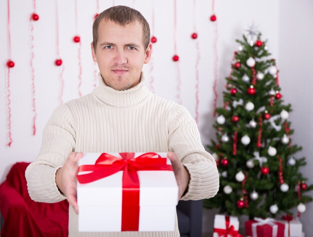 Happy young man giving christmas present box over christmas background
