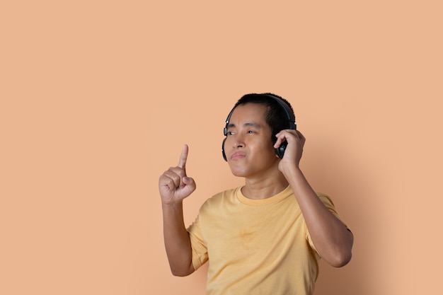 Happy young man in headphones listening to music and dancing on orange studio background. Listening music.