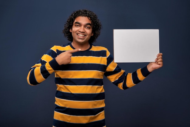 A happy young man holding and displaying a signboard or placard in his hands on a dark background ready for your text or product