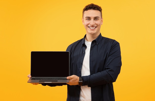 Happy young man holding laptop computer with black blank screen