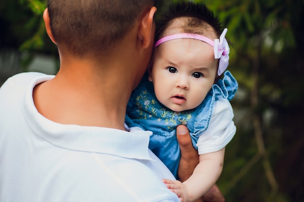 Happy young man holding a smiling 2-4 months old baby on a background of leaves not in focus