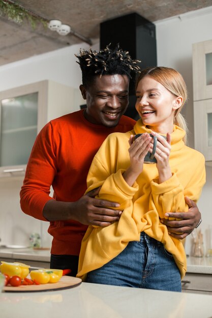 Happy young man laughing and hugging his beloved girlfriend while standing in the kitchen with her