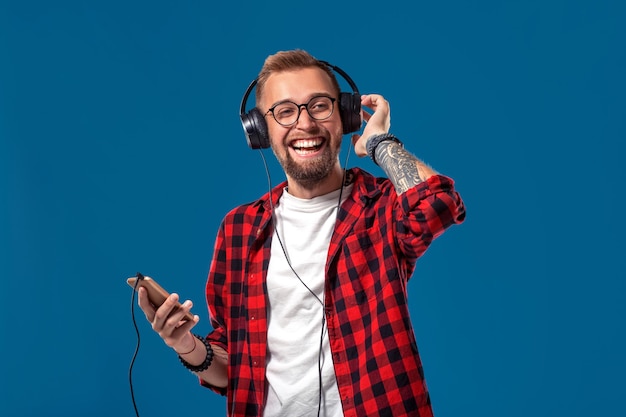 Happy young man listening to music with headphones handsome smiling guy in checkered shirt dancing w...