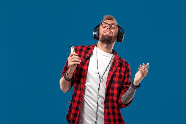 Happy young man listening to music with headphones handsome\
smiling guy in checkered shirt with clos...