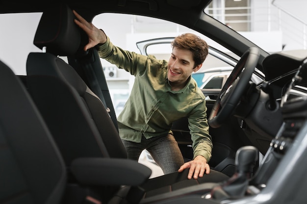 Happy young man looking inside car salon selecting new automobile at modern dealership