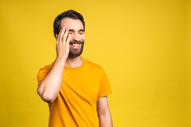 Happy young man. Portrait of handsome young bearded man in casual smiling while isolated over yellow background.