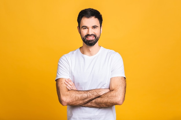 happy young man. portrait of handsome young man in casual keeping arms crossed and smiling while standing isolated over yellow background.