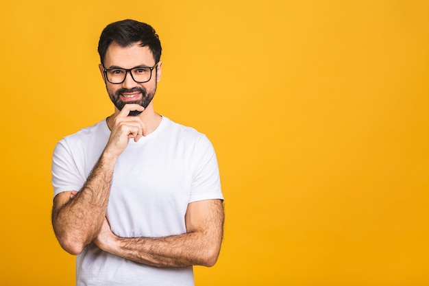 Happy young man. portrait of handsome young man in casual keeping arms crossed and smiling while standing isolated over yellow background