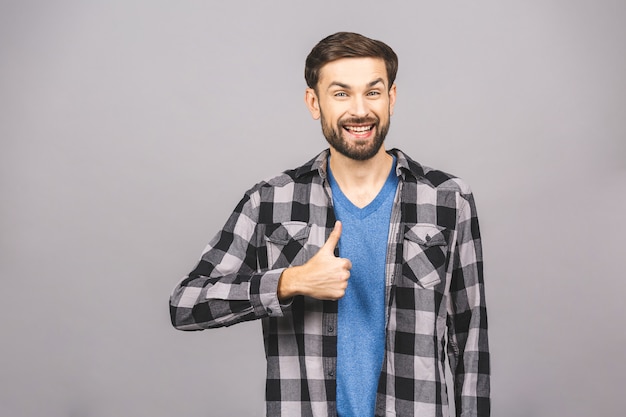 Happy young man. Portrait of handsome young man smiling while standing against gray white wall. Thumbs up.