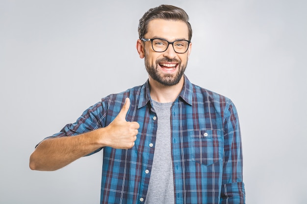 Happy young man. Portrait of handsome young man smiling while standing against white wall. Thumbs up.