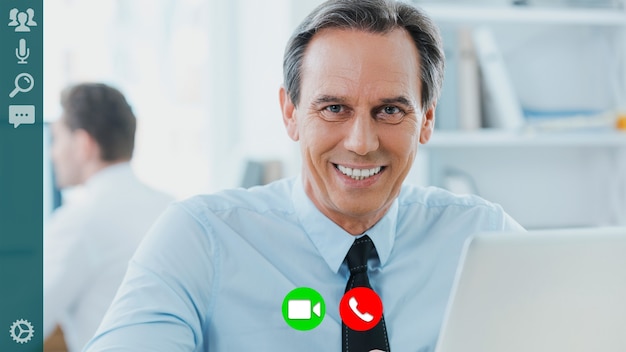 Happy young man in shirt and tie looking at camera and smiling while having video call