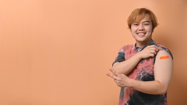 Счастливый молодой человек показывает свою руку с повязкой после вакцинации