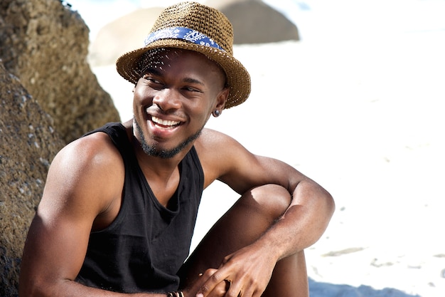 Happy young man sitting at the beach with hat